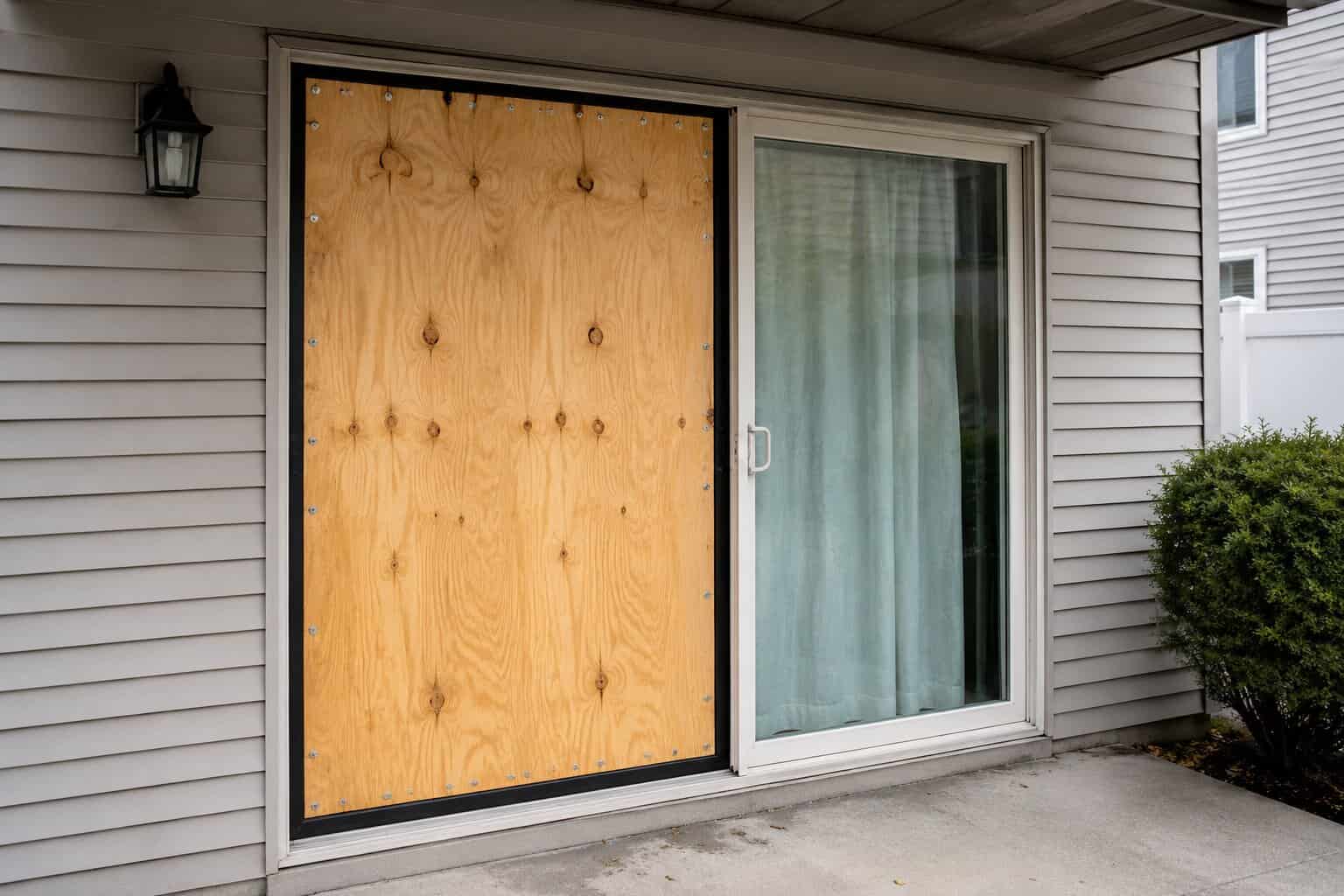 Plywood board-up installed over a broken sliding patio door opening on a home exterior