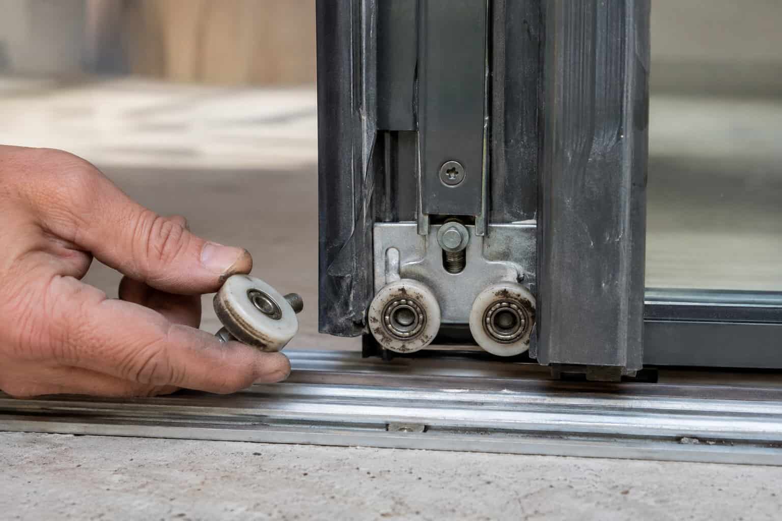 Close-up of a worn sliding glass door roller assembly being replaced